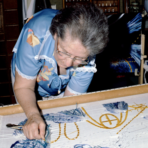 Volunteer Marjorie Biggs leaning over and embroidering the runner for the Caroline Herschel place setting