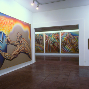 Color photograph of artworks installed on white walls in a gallery with another gallery visible through a doorway in the center