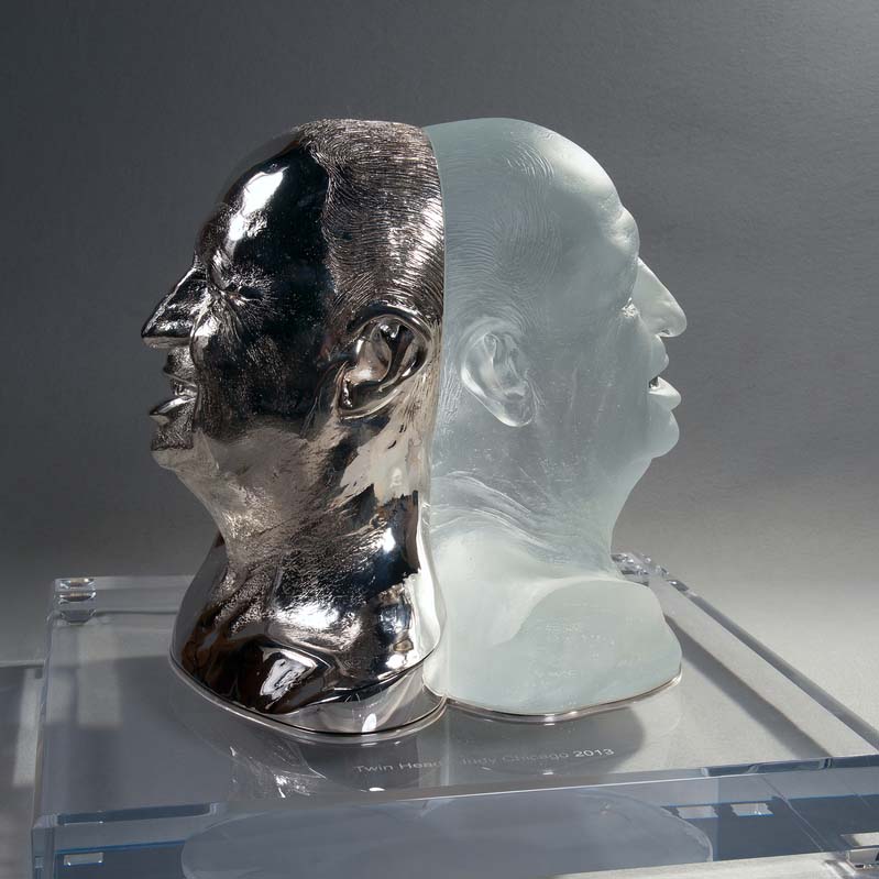 Translucent silver and white sculpture of two men's heads back to back on a clear plinth