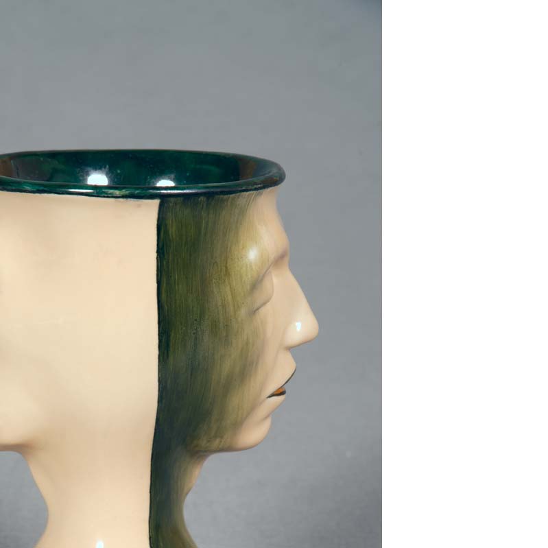 Mug in shades of dark green, and metallic gold with a face on either side and a flared base