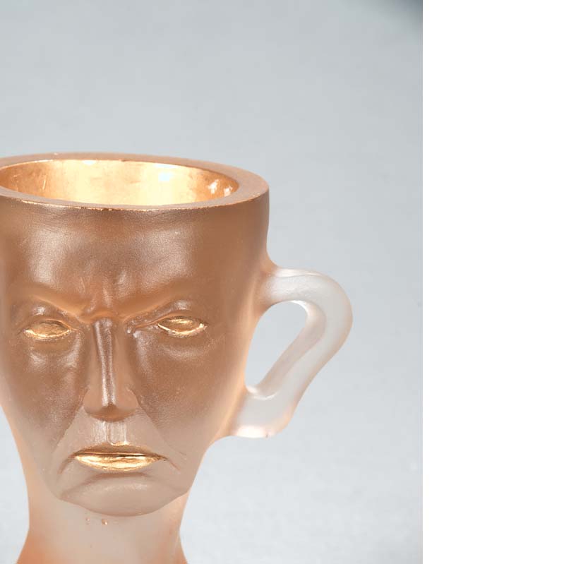 Mug in translucent white and gold with a frowning face and handle atop a flared base
