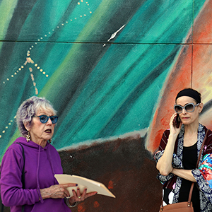 Color photograph of Judy Chicago and Jeanne Greenberg Rohatyn standing in front of a colorful mural