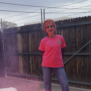 Color photograph of Judy Chicago standing behind a low stack of white blocks glowing pink