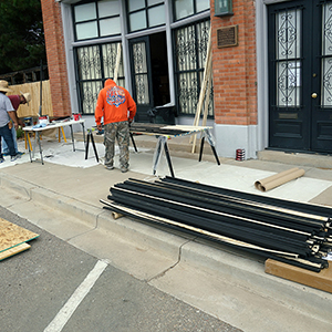 Color photograph of three people working with building supplies at tables set up on the sidewalk outside a brick building