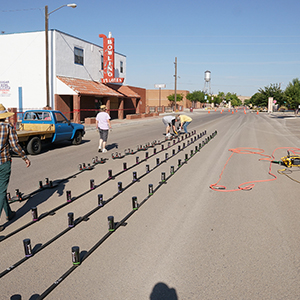 Color photograph of Ayrton Chapman, an unidentified woman, Jim Perry, and Larry Scripter installing four rows of smoke canisters in the middle of a paved street