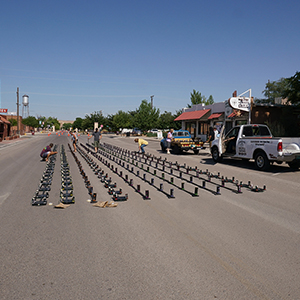 Color photograph of Chris Souza, Mary Costa, an unknown man, and Larry Scripter installing ten rows of smoke canisters in the middle of a paved street