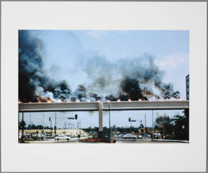 Print of black smoke rising from lit flares on a bridge over a city street