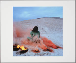 Print of a green-skinned woman sitting in a desert landscape with orange and a fire at her feet