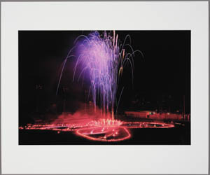 Print of a butterfly shape outlined in orange flares on a black ground with purple fireworks rising from it