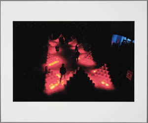 Print of small figures silhouetted against two rows of glowing, red, pyramidal forms