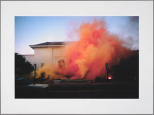 Print of a orange smoke rising in front of a beige building