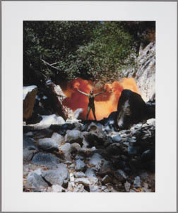 Print of a woman standing with her arms spread in a rocky canyon with orange smoke billowing behind her