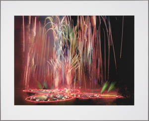 Print of an outline of a butterfly in multi colored flares on the ground with fireworks erupting from it