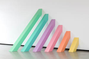 Increasingly smaller painted stainless steel beams leaning against a wall arranged in order of the colors of the rainbow