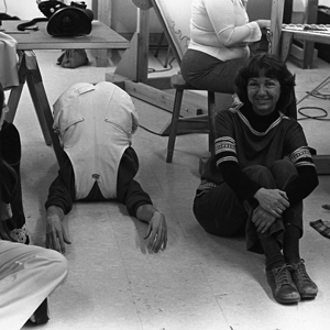 Three volunteers sitting on a studio floor with the center volunteer’s body flipped over backwards over her arms