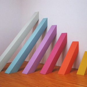 Six columnar trapezoids, each of a different length and color leaning against a wall in decreasing order of size