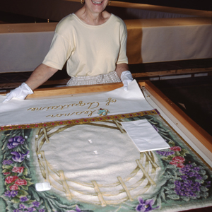 Volunteer Audrey Cowan smiling and holding with white gloves the runner for the Eleanor of Aquitaine place setting