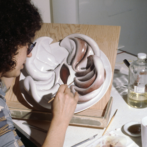 Judy Chicago paints half of the plate for Susan B. Anthony that is propped up on an easel.