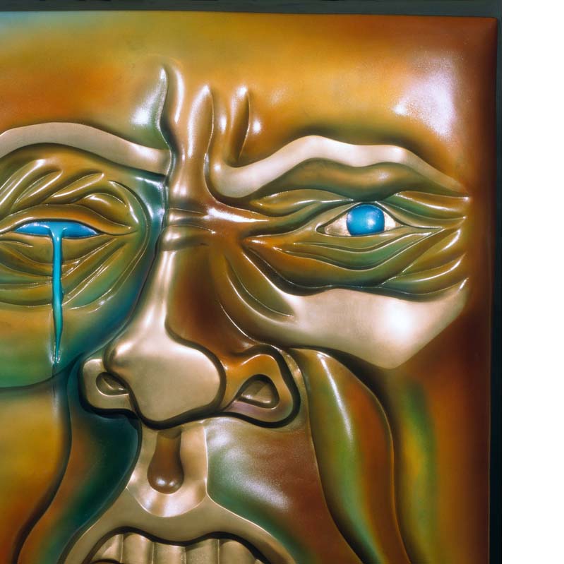 Relief sculpture of a wrinkled face in shades of orange and turquoise with a tear dripping from a missing eye and an open mouth