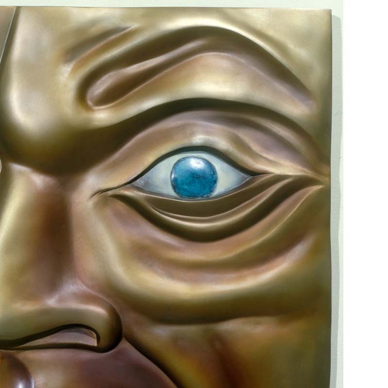 Relief sculpture in shades of gold, brown, and turquoise of a partial, wrinkled face with an open mouth