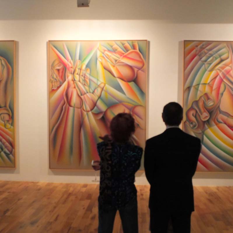 Color photograph of two people standing in front of three large rainbow-colored paintings