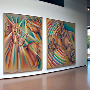 Panoramic color photograph of artworks on the walls of a gallery with a few people standing at the entrance