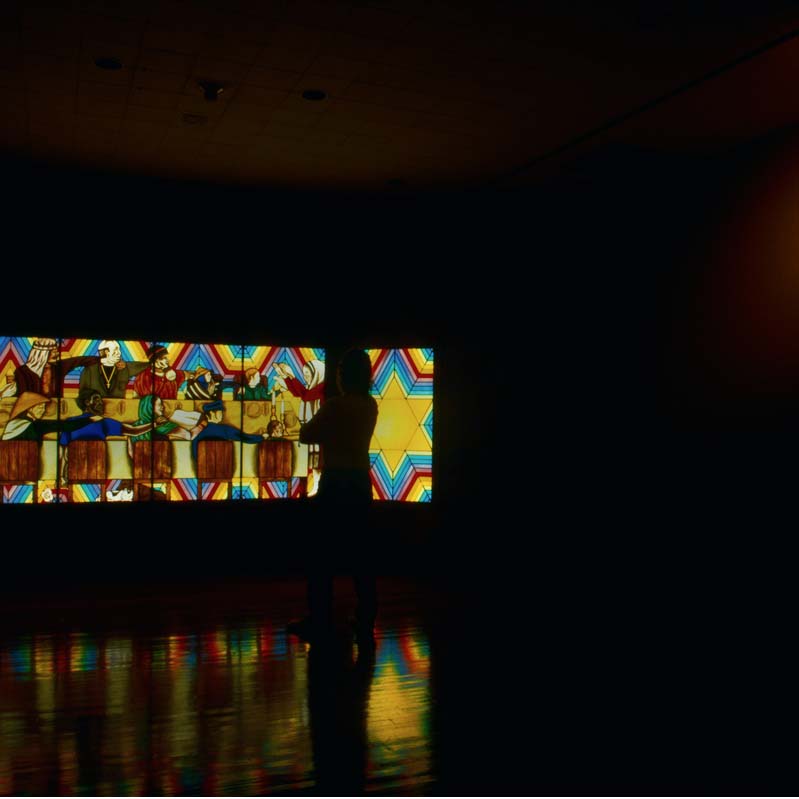 Color photograph of a glowing stained glass work in a darkened gallery