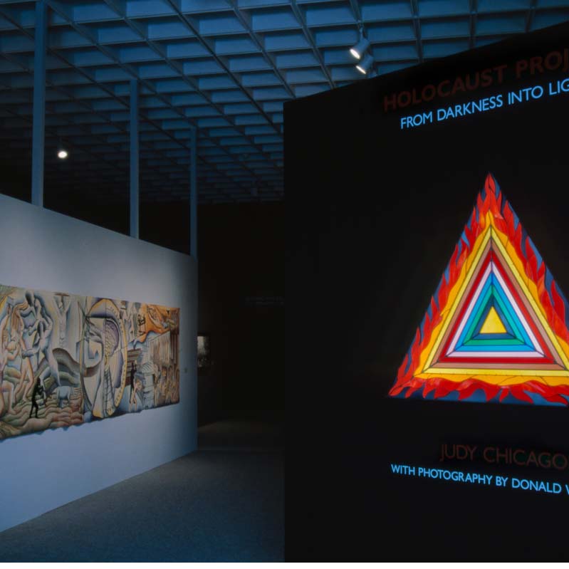 Color photograph of a painting and a stained glass work in a darkened gallery