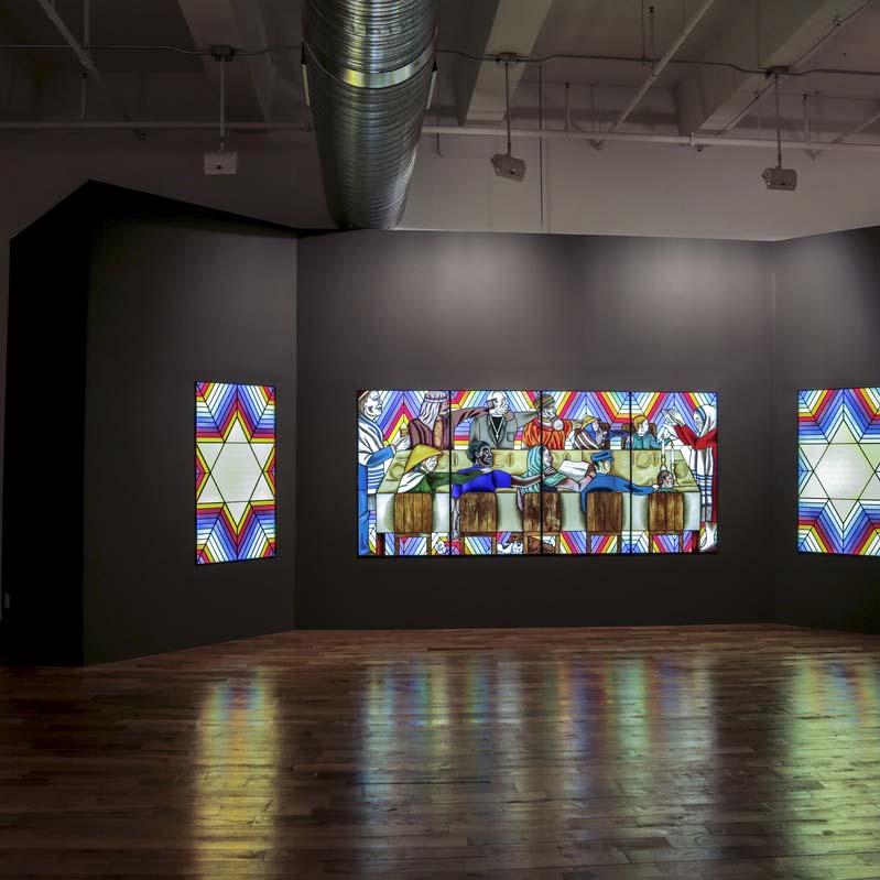 Color photograph of a glowing stained glass work embedded in a wall in a darkened gallery