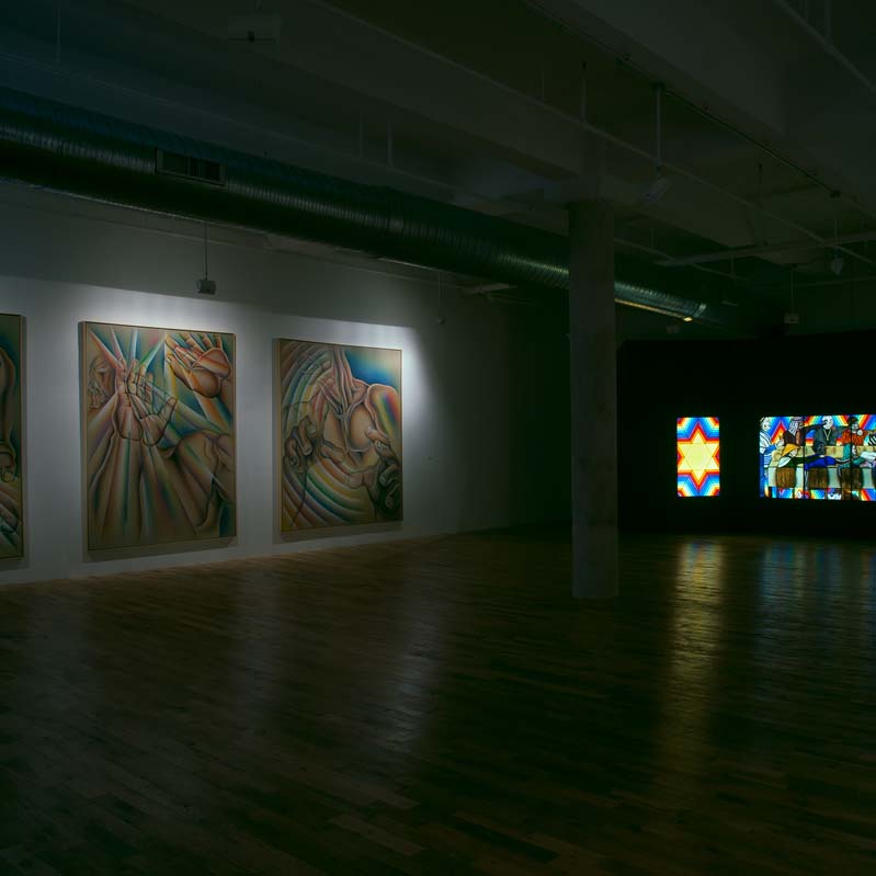 Color photograph of three paintings and a stained glass work in a darkened gallery