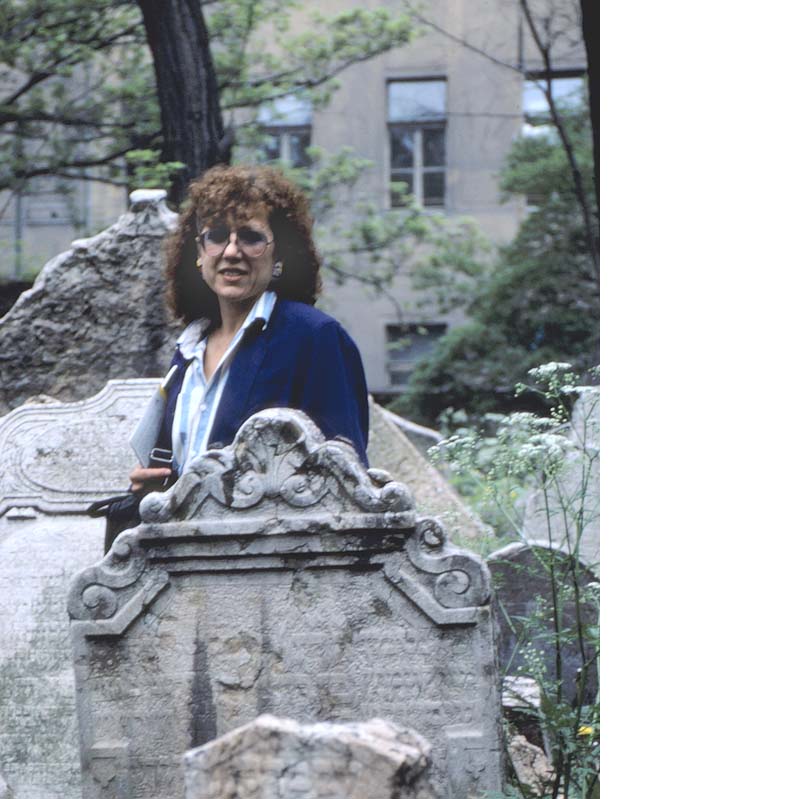 Color photograph of Judy Chicago standing amid crooked gravestones