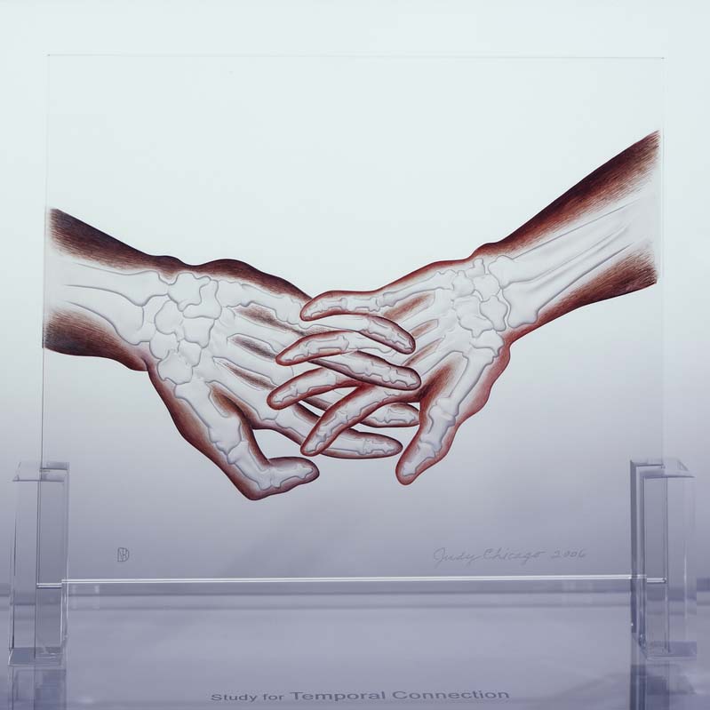 Sculpture of two hands holding hands with exposed bones painted on a clear rectangle on a clear plinth