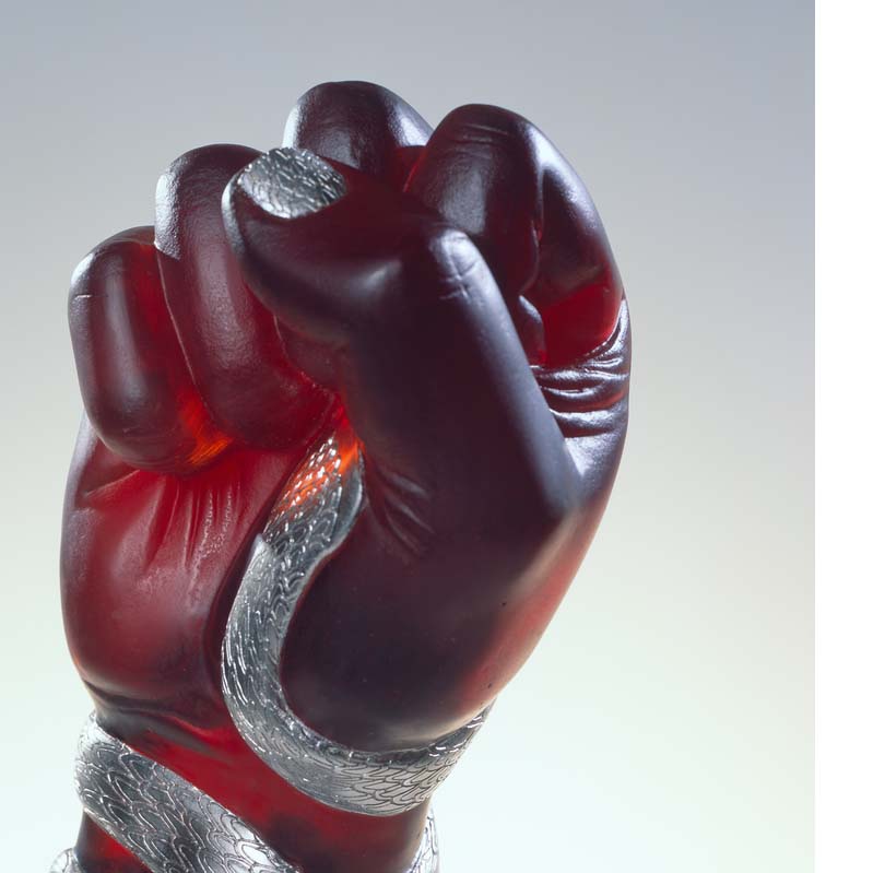 Detail of a sculpture of a translucent red raised fist with a silver snake coiled around the arm