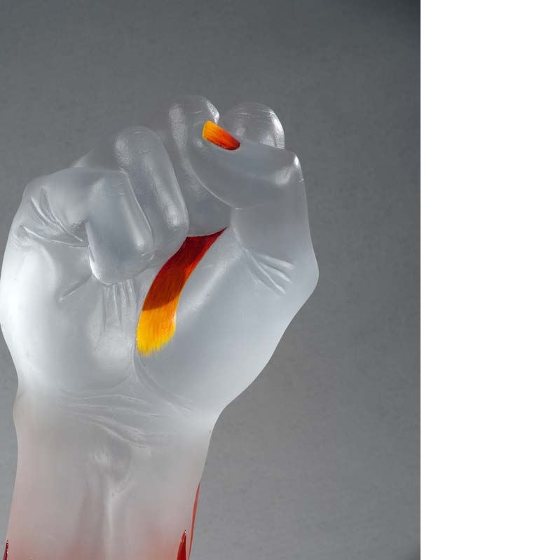 Detail of a sculpture of a translucent white raised fist with yellow and red details on the hand and flames on the arm