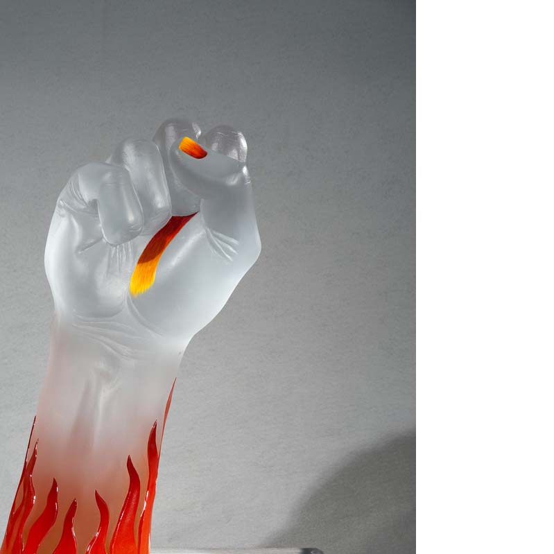 Sculpture of a translucent white raised fist with yellow and red details on the hand and flames on the arm on a clear plinth