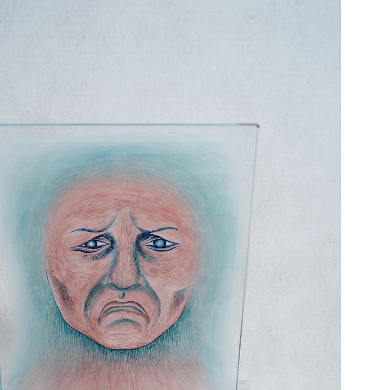 Pink and turquoise painting of a frowning face on a clear glass rectangle on a clear plinth