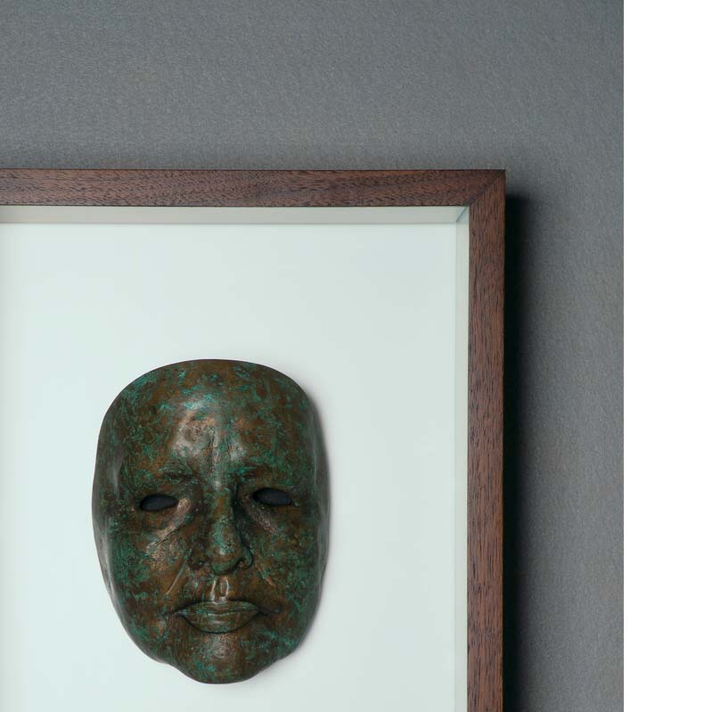 Brown and green relief sculpture of a face framed on a white background