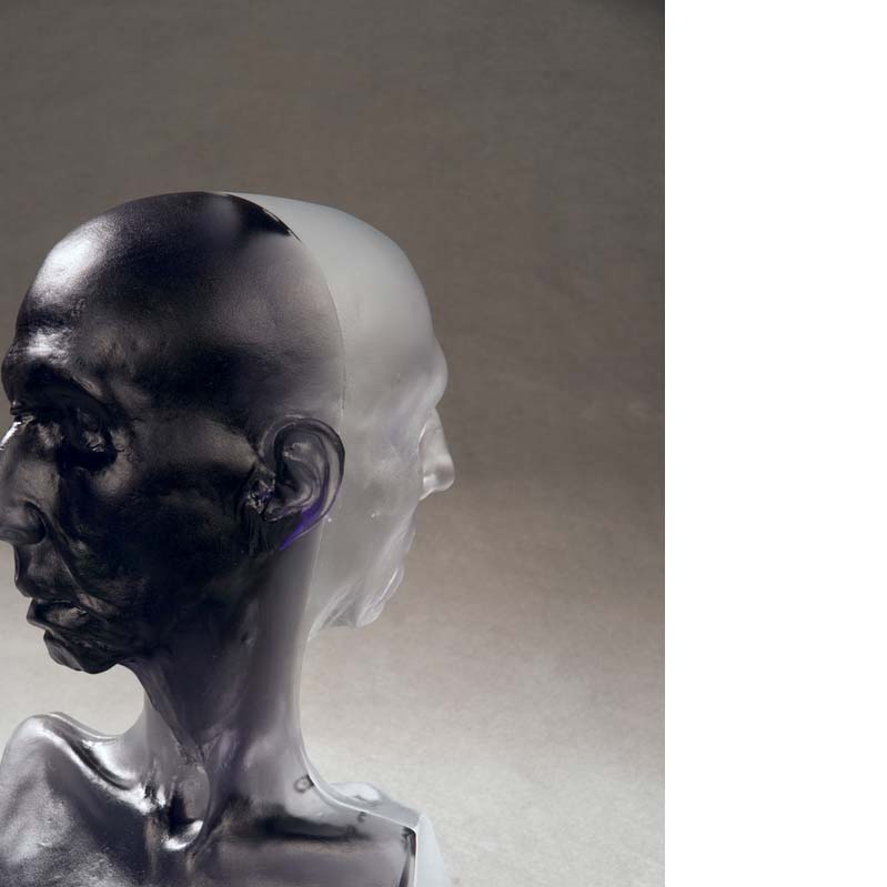 Sculpture of a bust with two bald heads, back to back One head is black; the other is translucent white