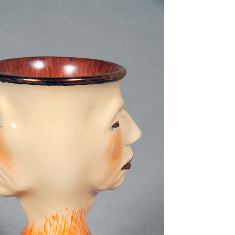 Mug in earth tones with a face on either side and a flared base