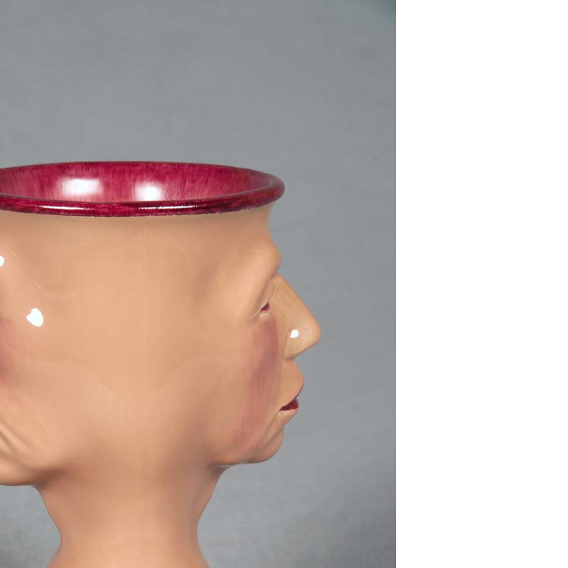 Mug in shades of peach and dark pink with a face on either side and a flared base