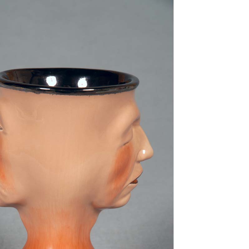 Mug in shades of orange and black with a face on either side and a flared base