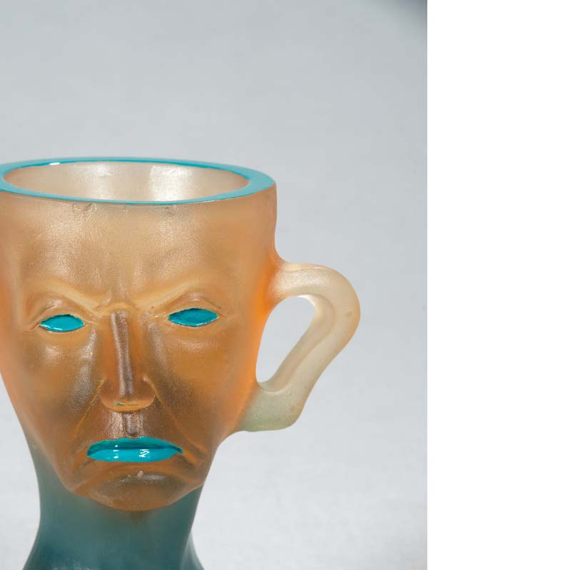 Mug in translucent orange and turquoise with a face, handle, and a flared base