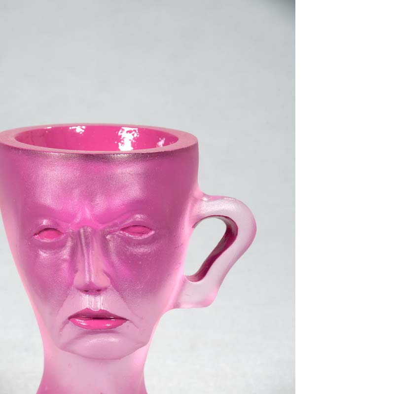 Mug in translucent pink with a frowning face and handle atop a flared base
