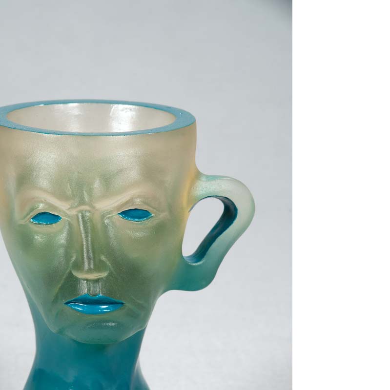 Mug in translucent turquoise with a face, handle, and a flared base