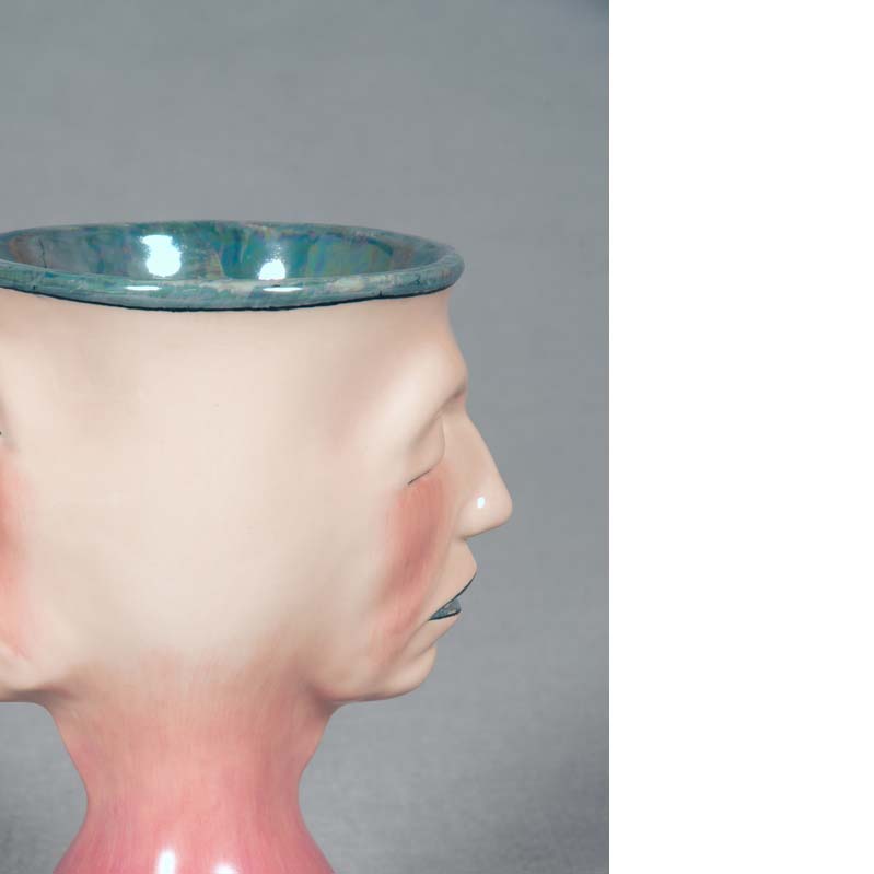 Mug in shades of pink and turquoise with a face on either side and a flared base