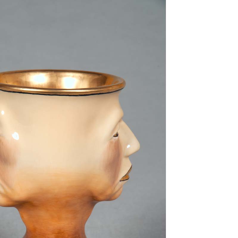 Mug in shades of brown, beige, and metallic gold with a face on either side and a flared base