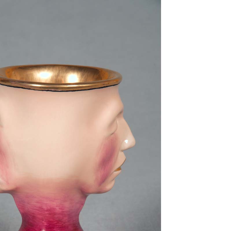 Mug in shades of pink, beige, and metallic gold with a face on either side and a flared base