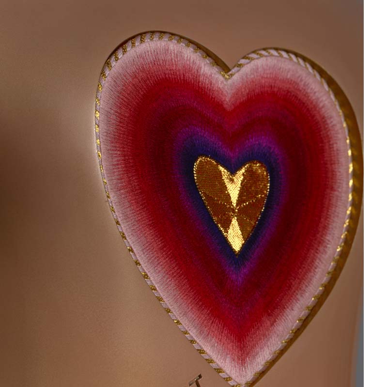 Red, purple, and gold embroidery heart mounted on a curving beige surface with gold text
