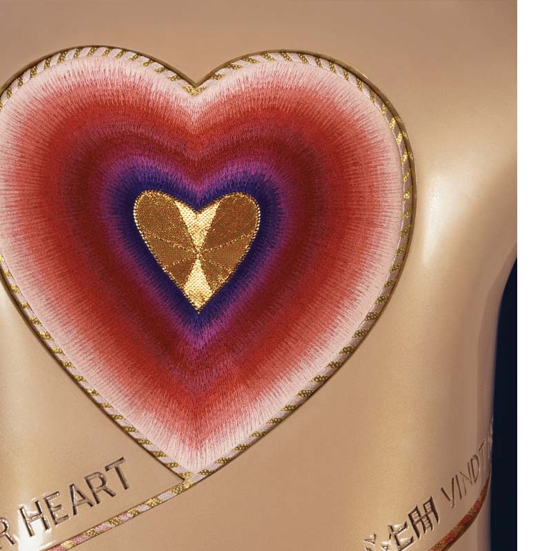 Red, purple, and gold embroidery heart mounted on a curving beige column with gold text