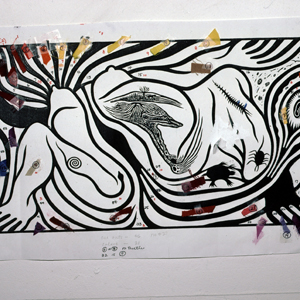 Black and white pattern of a squatting woman figure with flowing hair giving birth to an embryo and surrounded by animals. The pattern is hung up by pushpins and various color samples are pinned on top of it.